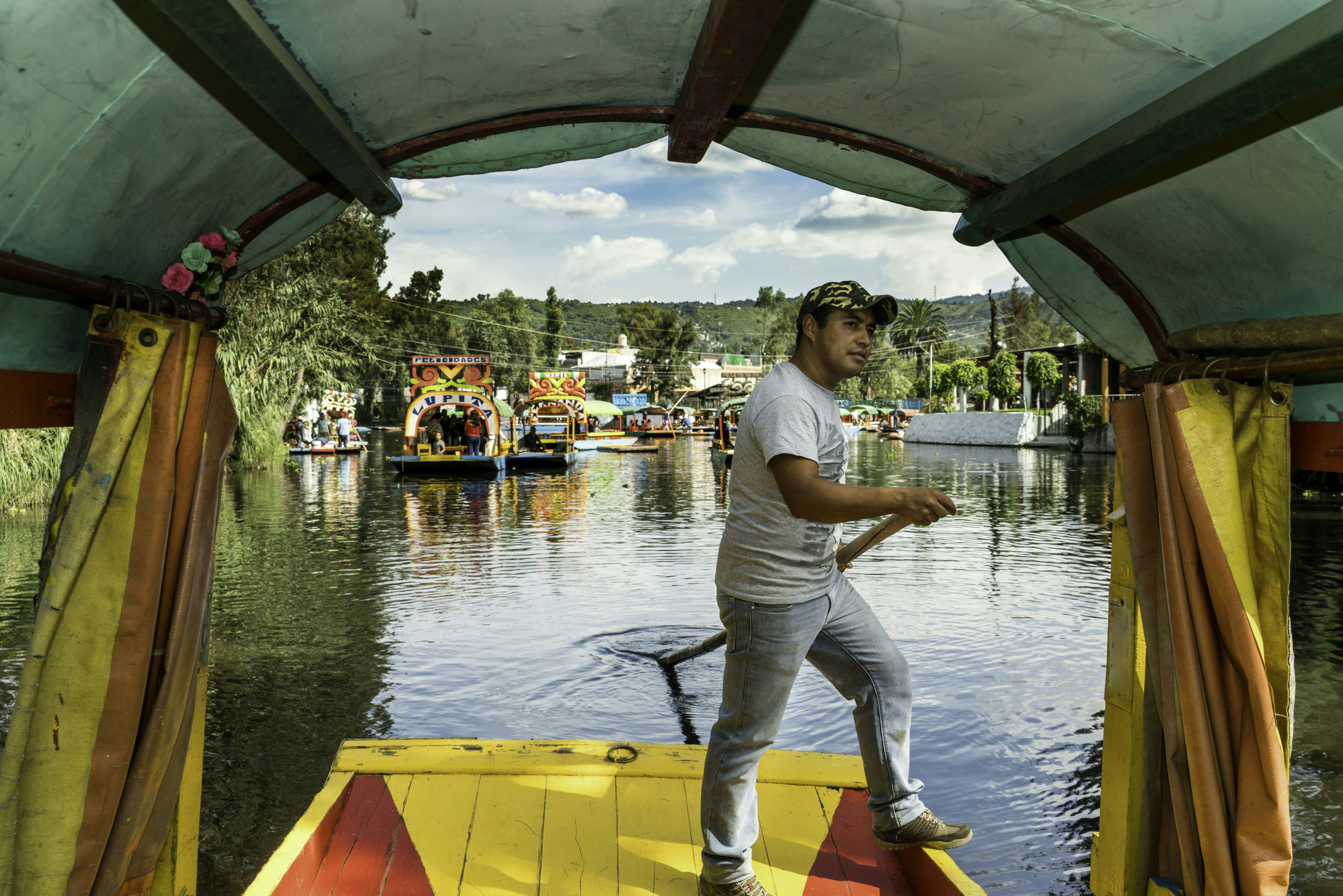 Vyras plaukia valtimi, vadinamu trajinera ant Xochimilco kanalų Meksike