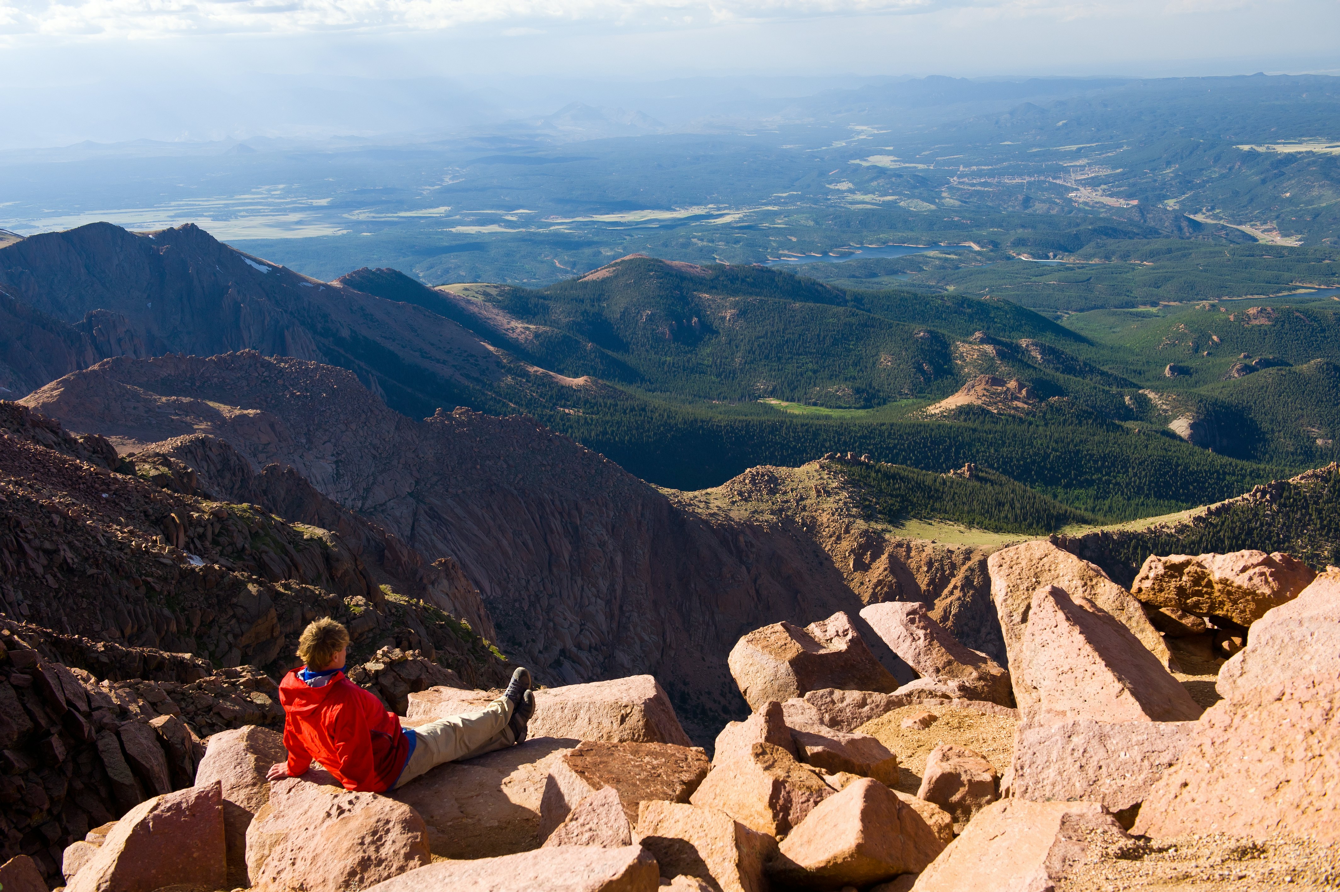 Jaunas keliautojas vyras, mėgaujantis vaizdingu vaizdu iš „Pikes Peak“ gražioje, saulėtoje dieną, spardydamas ant šiltų saulėtų uolų, kai kojos ištiestos priekyje.