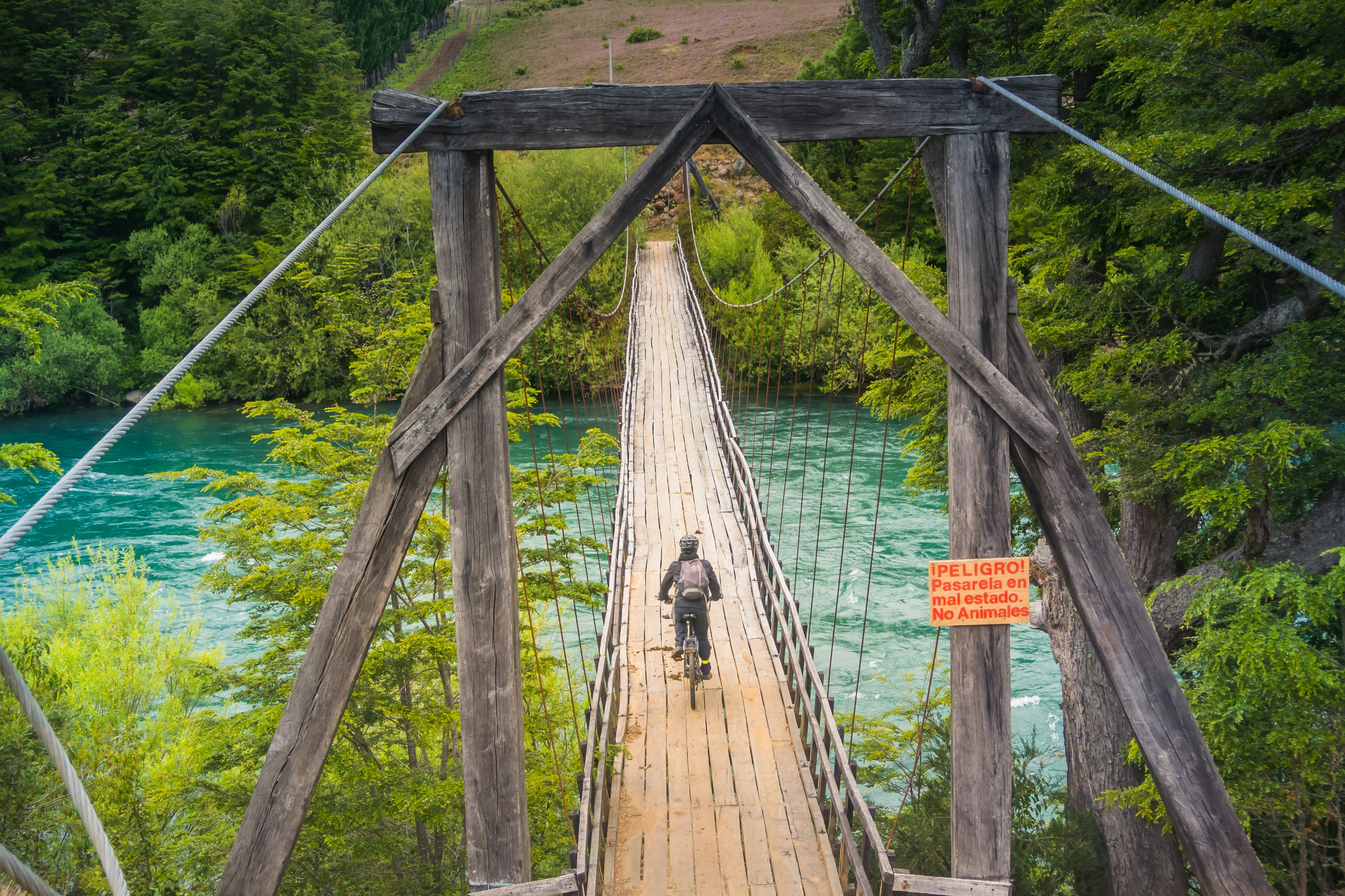 Asmuo ant dviračio kerta medinį tiltą Futaleufu mieste, Patagonijoje Čilėje.