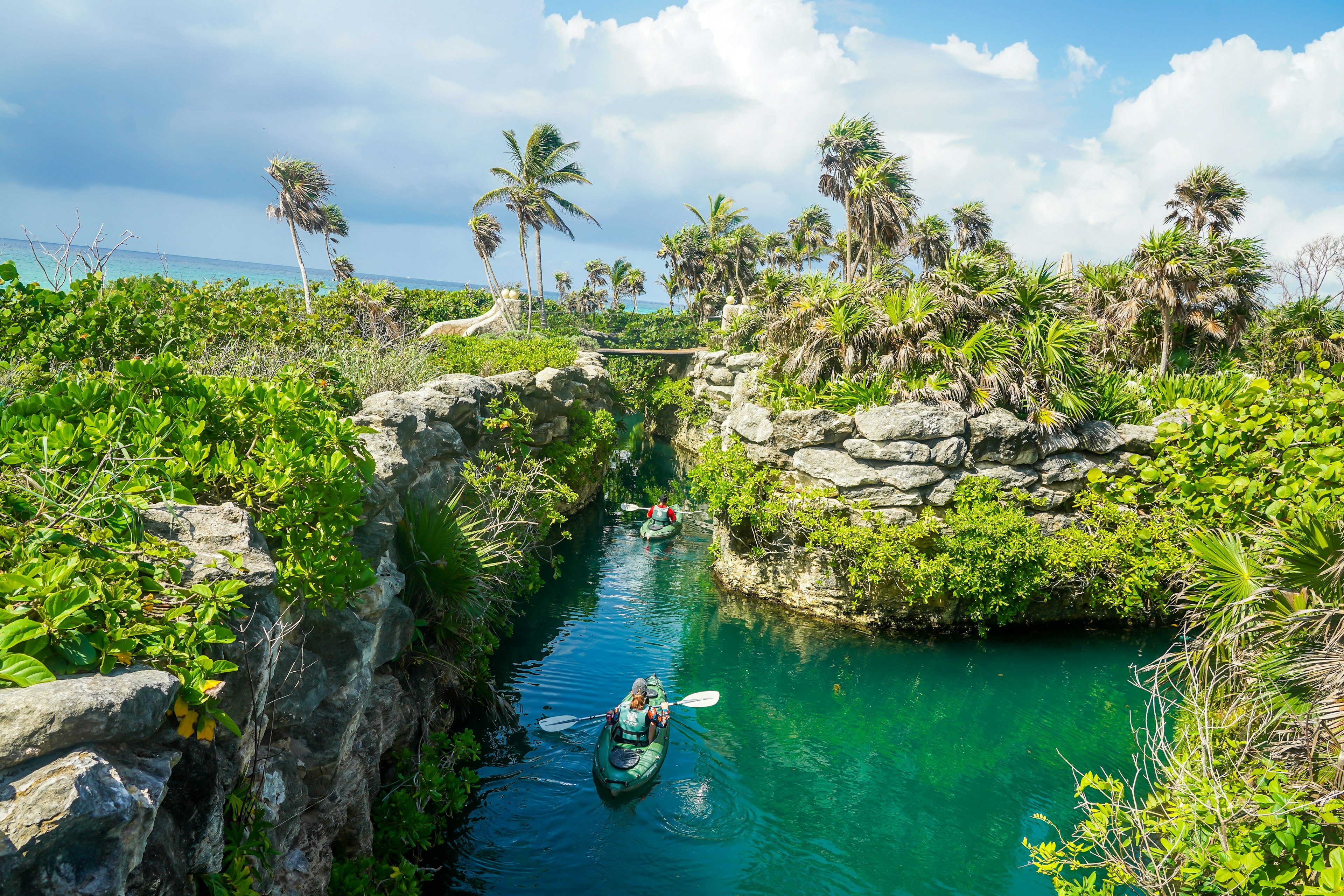 Žmogus baidarėmis kanale per akmenuotas sienas ir žalias džiungles „Xcaret“, Playa del Carmen, Meksikoje
