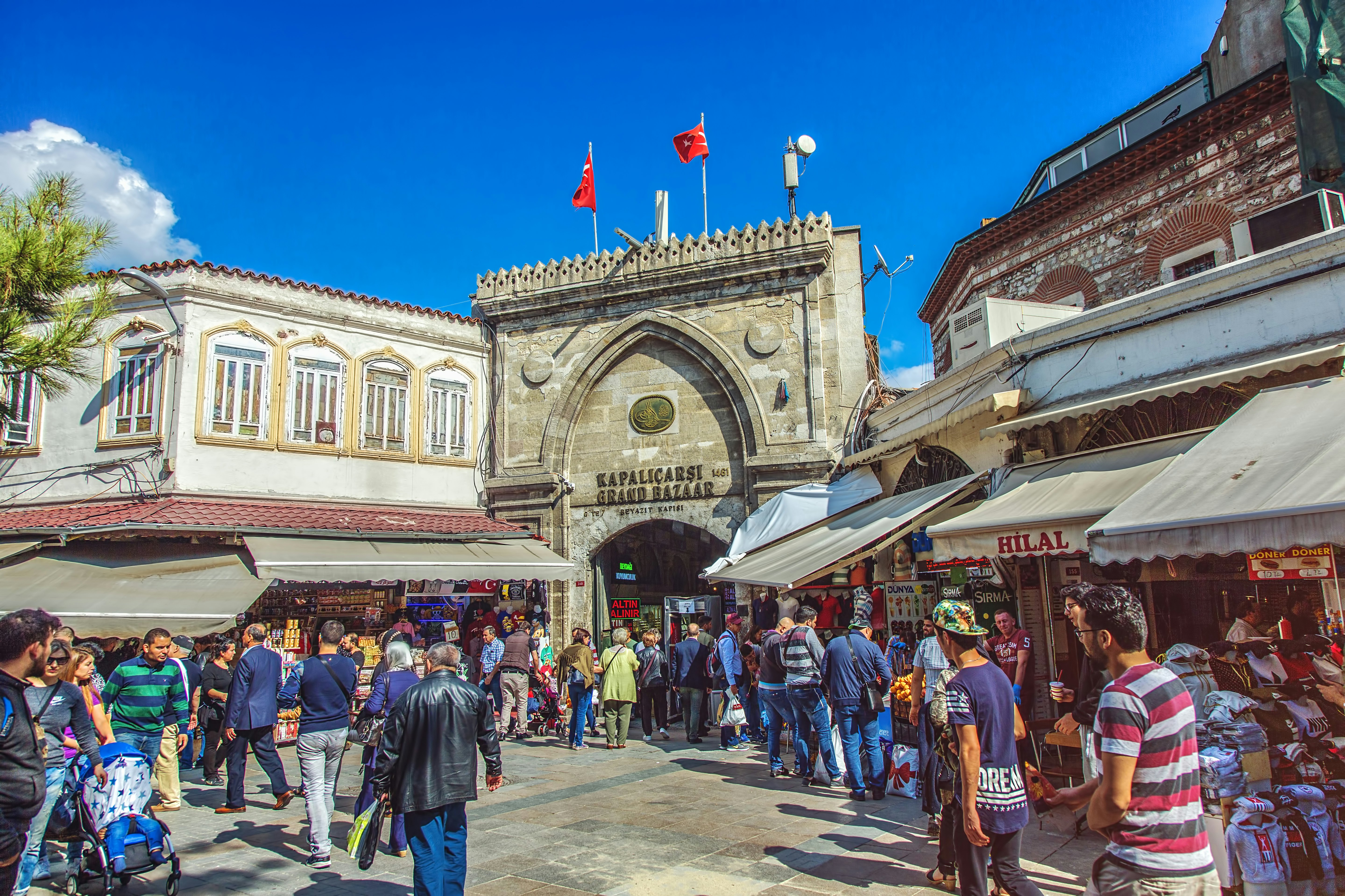 Rinkos kioskų serija šalia judrių vartų, kurių ženklas virš jo, kuriame sakoma "„Kapalcarsi Grand Bazaar“"