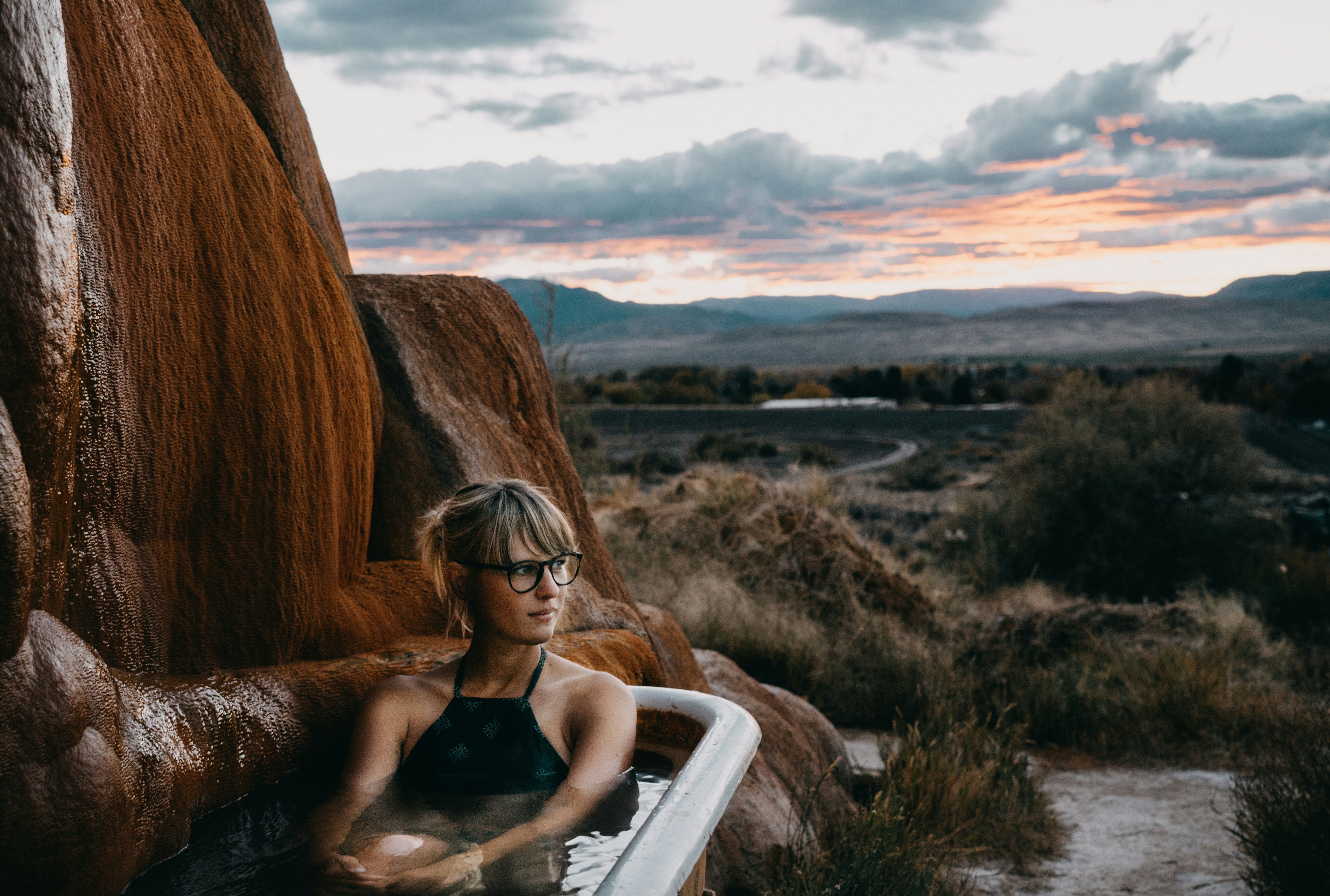 Moteris, sėdinti karštų šaltinių vonioje „Mystic Hot Springs“ Juta saulėlydžio metu