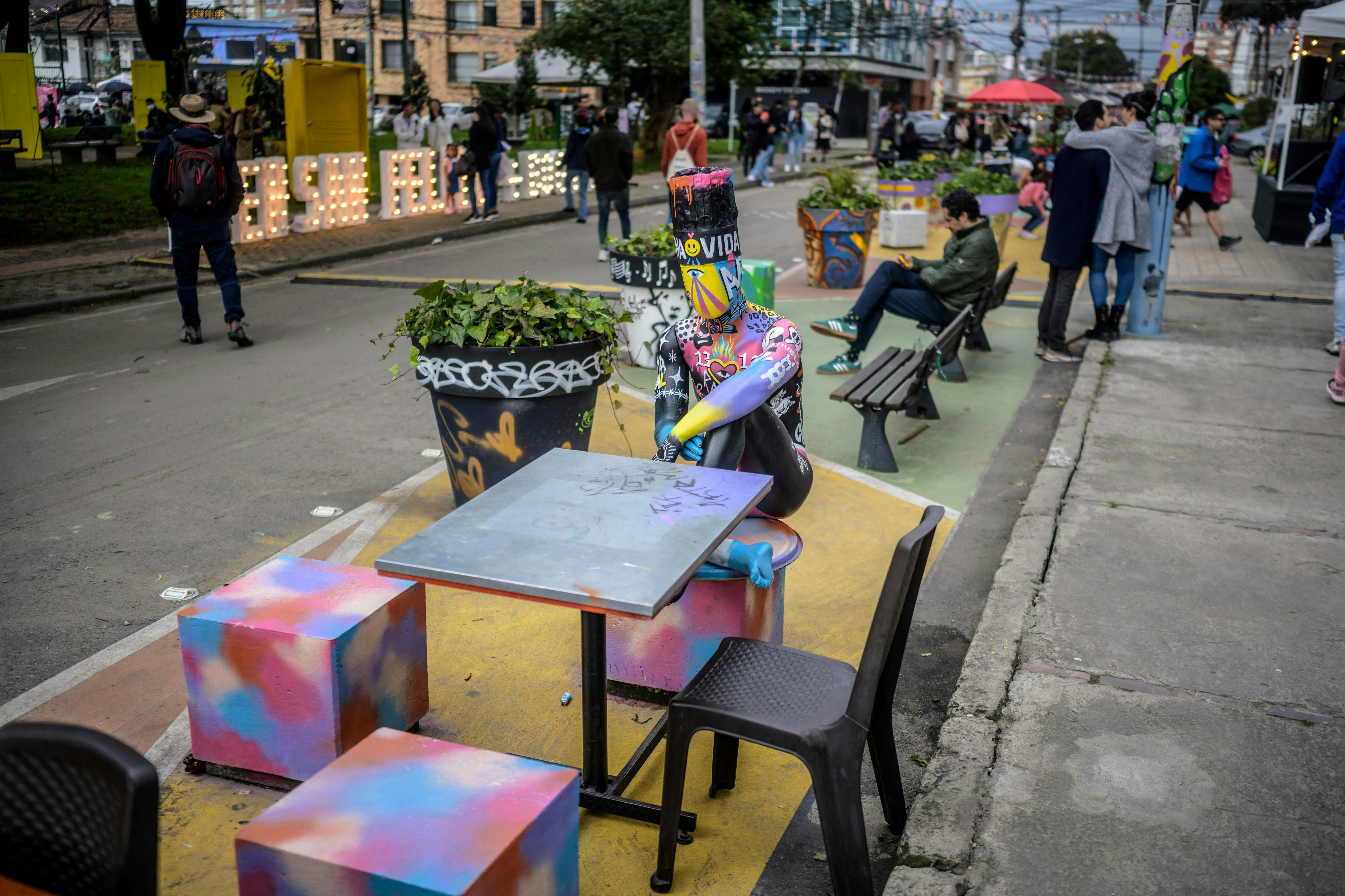 Žmonės pravažiuoja gatvę, papuoštą dažytomis kėdėmis ir stalais, skirtas atviram San Felipe festivaliui Bogotoje, Kolumbijoje