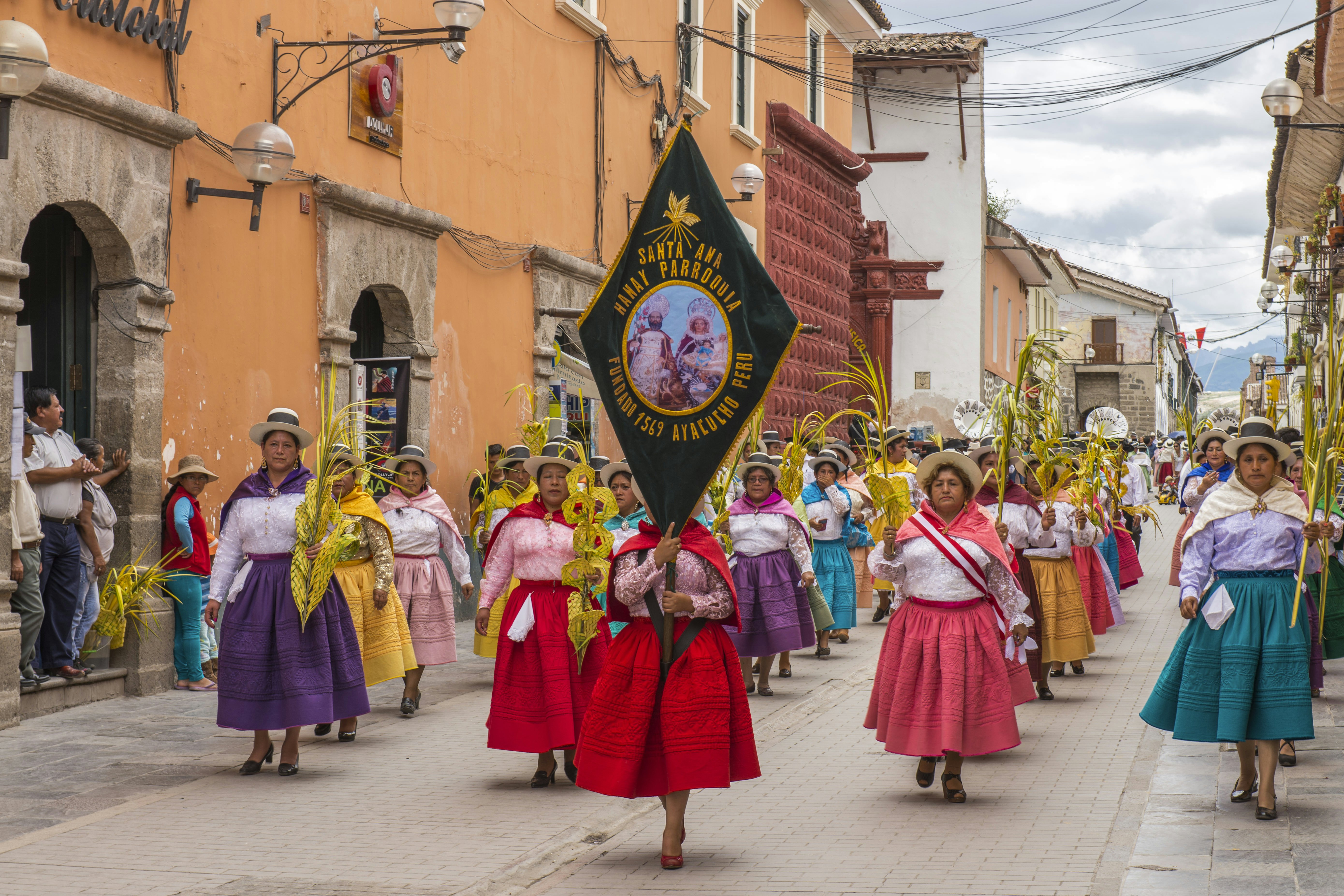 Žmonės su įvairiaspalvėmis suknelėmis ir skrybėlėmis, žygiuojančiais per Velykų Palmių sekmadienį Ayacucho mieste, Peru