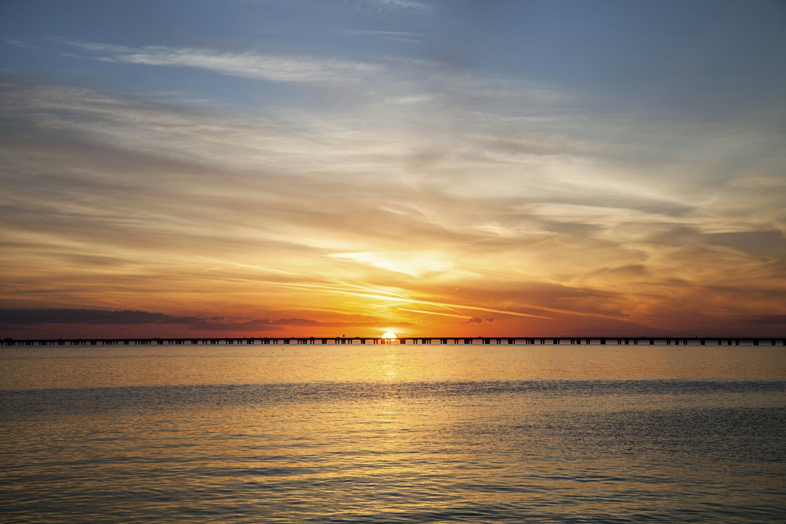 Spalvingas saulėlydis, kuriame vaizduojamas Luizianos ežeras Pontchartrain Causeway.