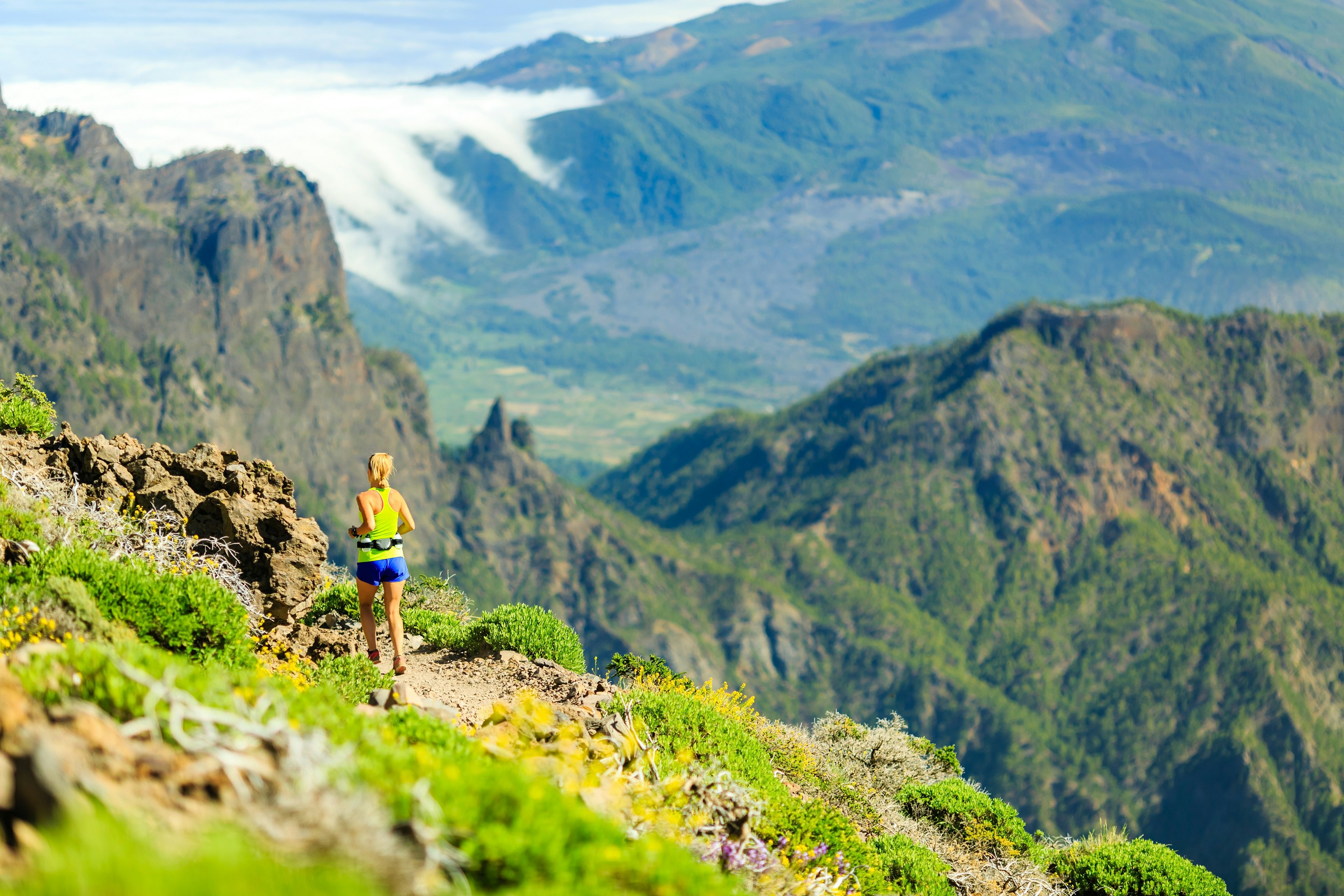 Young woman running or power walking in mountains on sunny summer day.