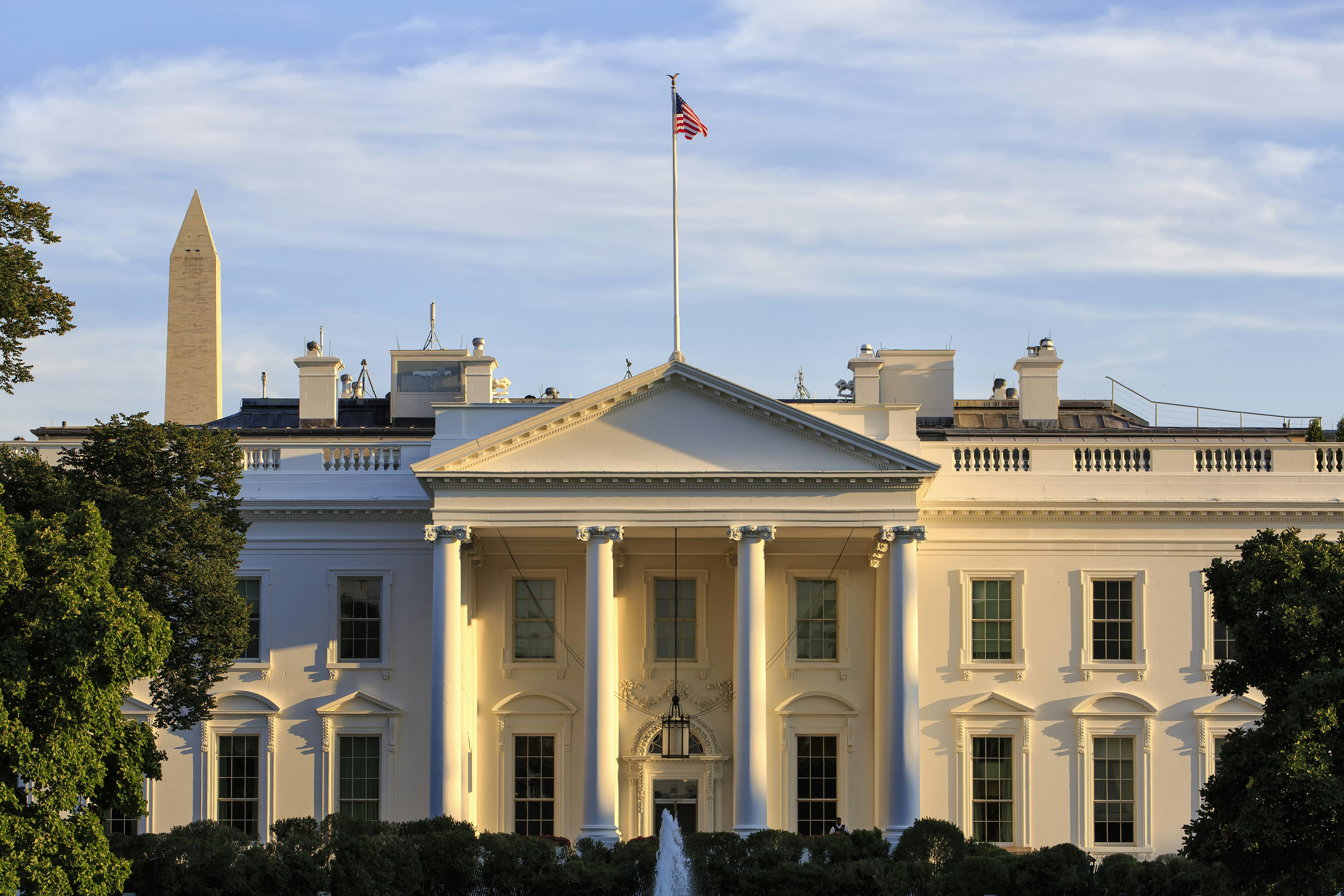 Exterior of the White House -- a large symmetrical colonnaded property with an American flag flying above it