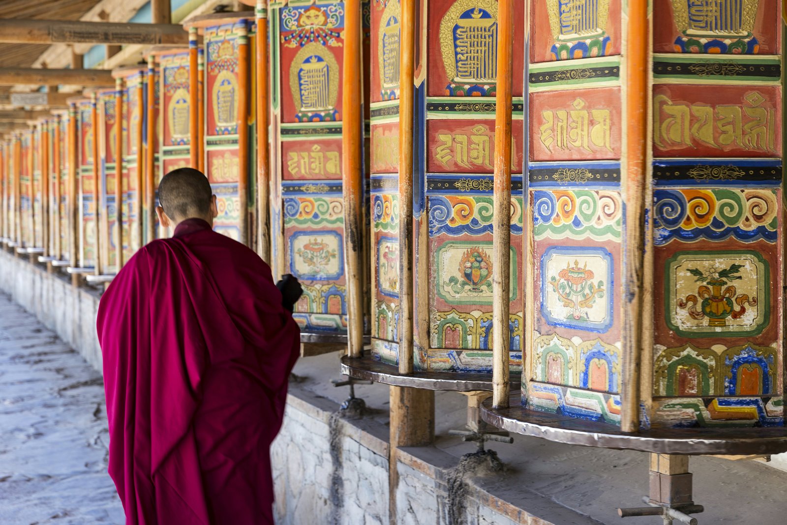 Vienuolis vaikšto ir paverčia didžiulius, spalvingus maldos ratus Labrango vienuolyne Xiahe, Gansu provincijoje.