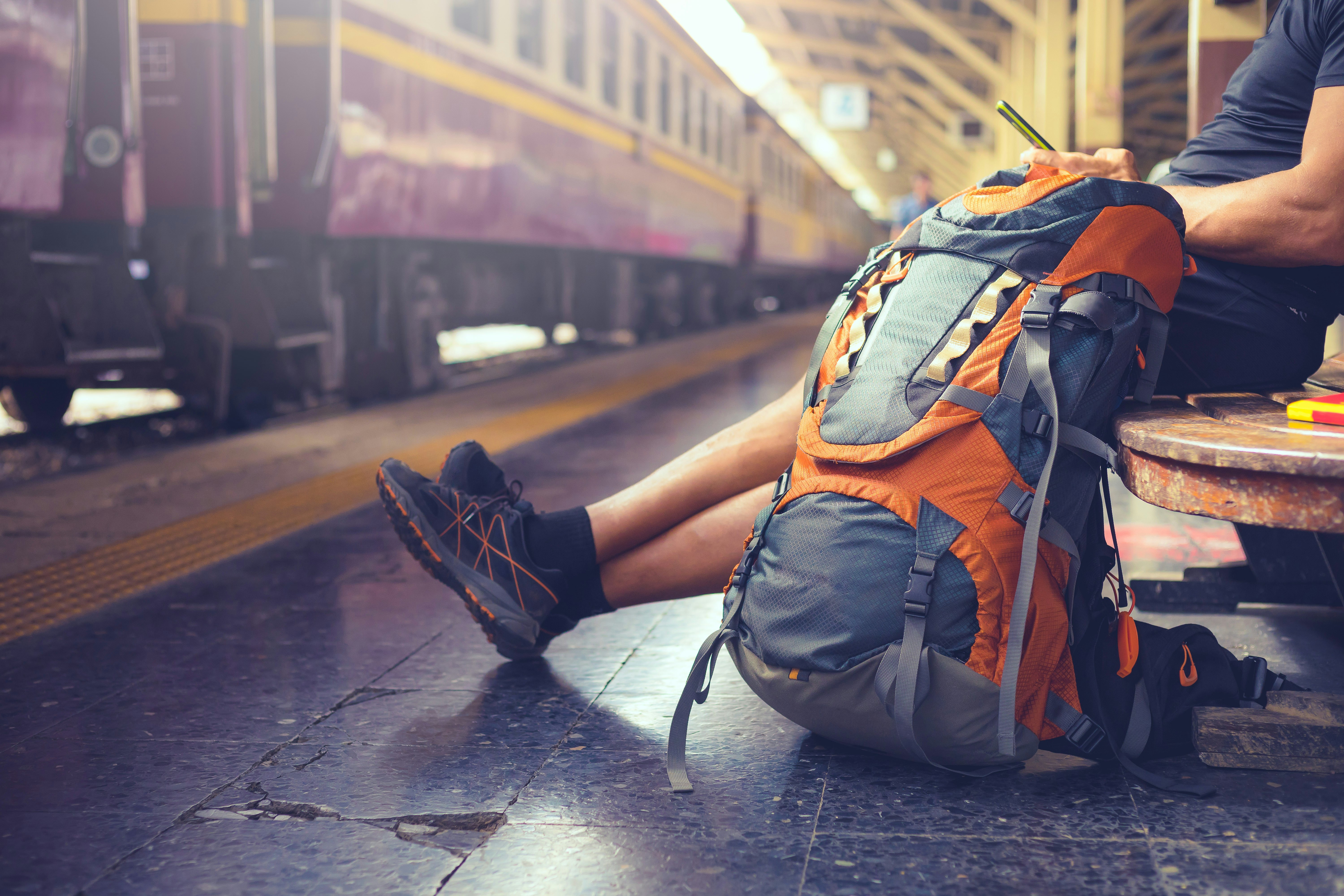 Backpackeris naudoja mobilųjį telefoną geležinkelio stotyje, laukdamas traukinio