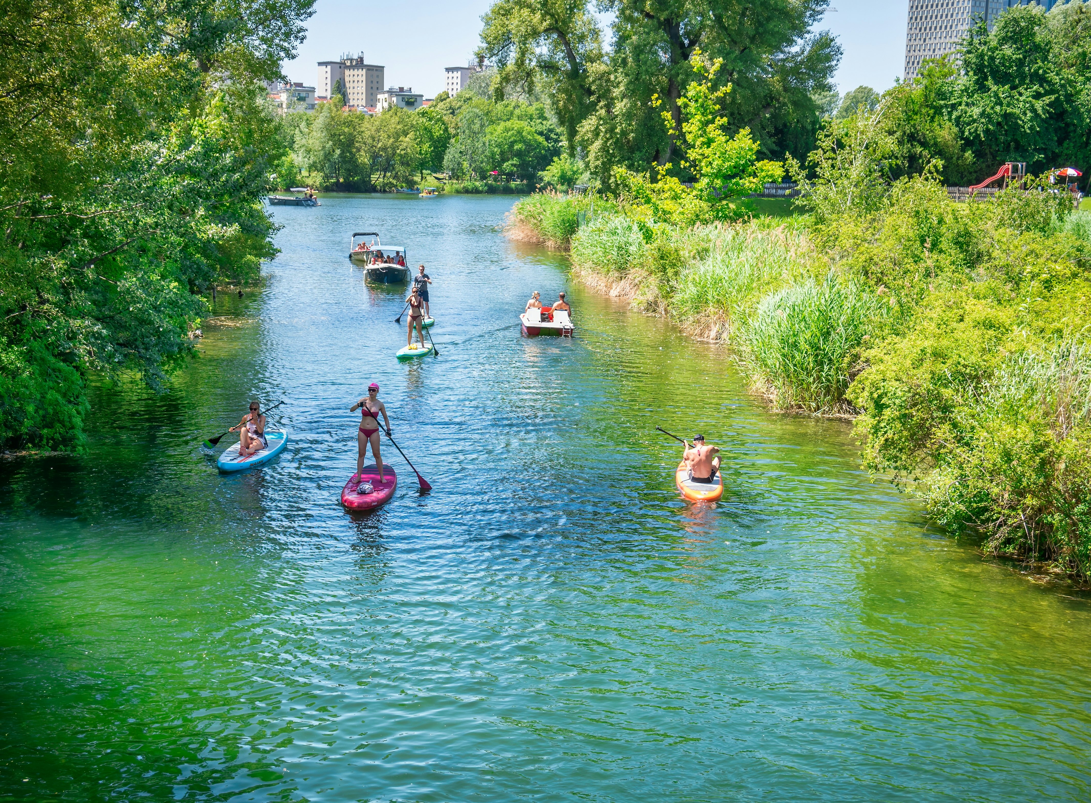Viena, Austrija - 2022 m. Birželio mėn.: Vasaros kraštovaizdis paplūdimyje su žmonėmis, kurie irklavo baidarėse ir stovi lentomis Kaiserwasser Alte Donau parke (Strandbad Gansehaufel)