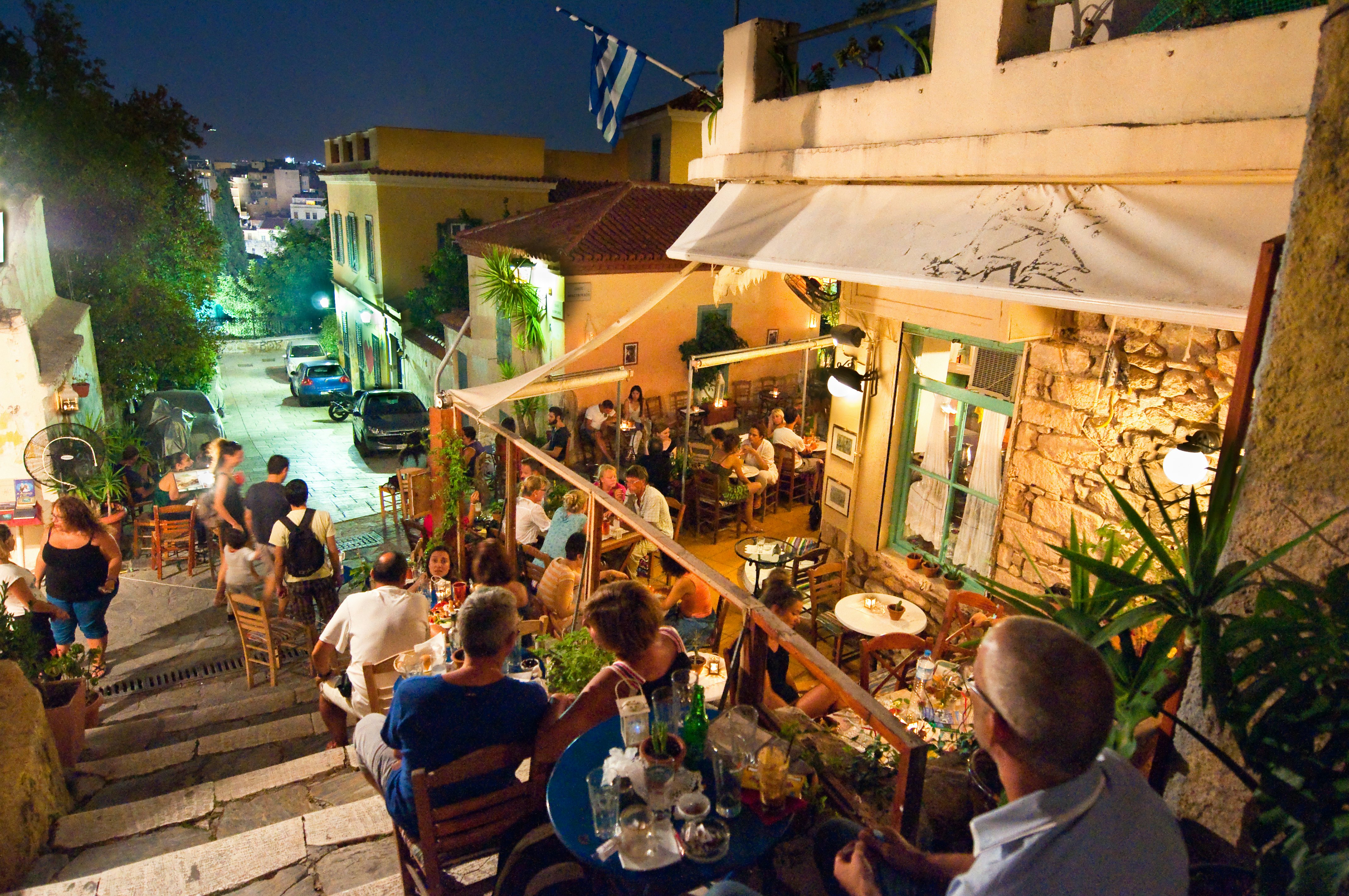 Atėnų Plakos rajone Graikijoje gatvėje alsuoja įvairūs restoranai ir barai, nes vietiniai gyventojai ir turistai mėgaujasi savo maistu naktį.