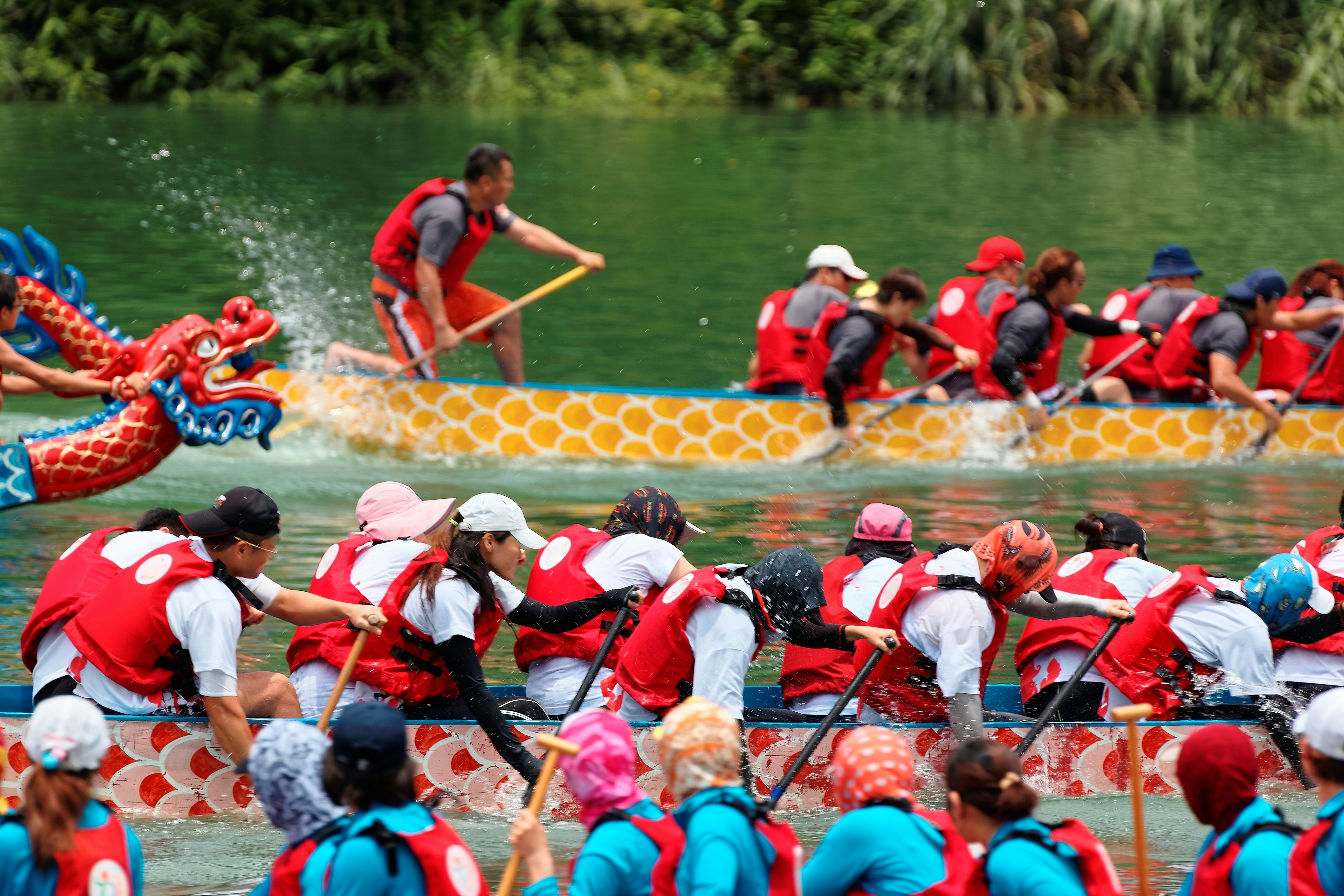 Konkurencingų valčių lenktynių „Dragon Boat“ festivalyje Taipėjuje, Taivane, scena, iš kurios atsiveria vaizdas į sportininkus, energingai traukiančius ant irklų ir griežtai konkuruojančiai tradiciniuose spalvinguose drakonų valtyse.