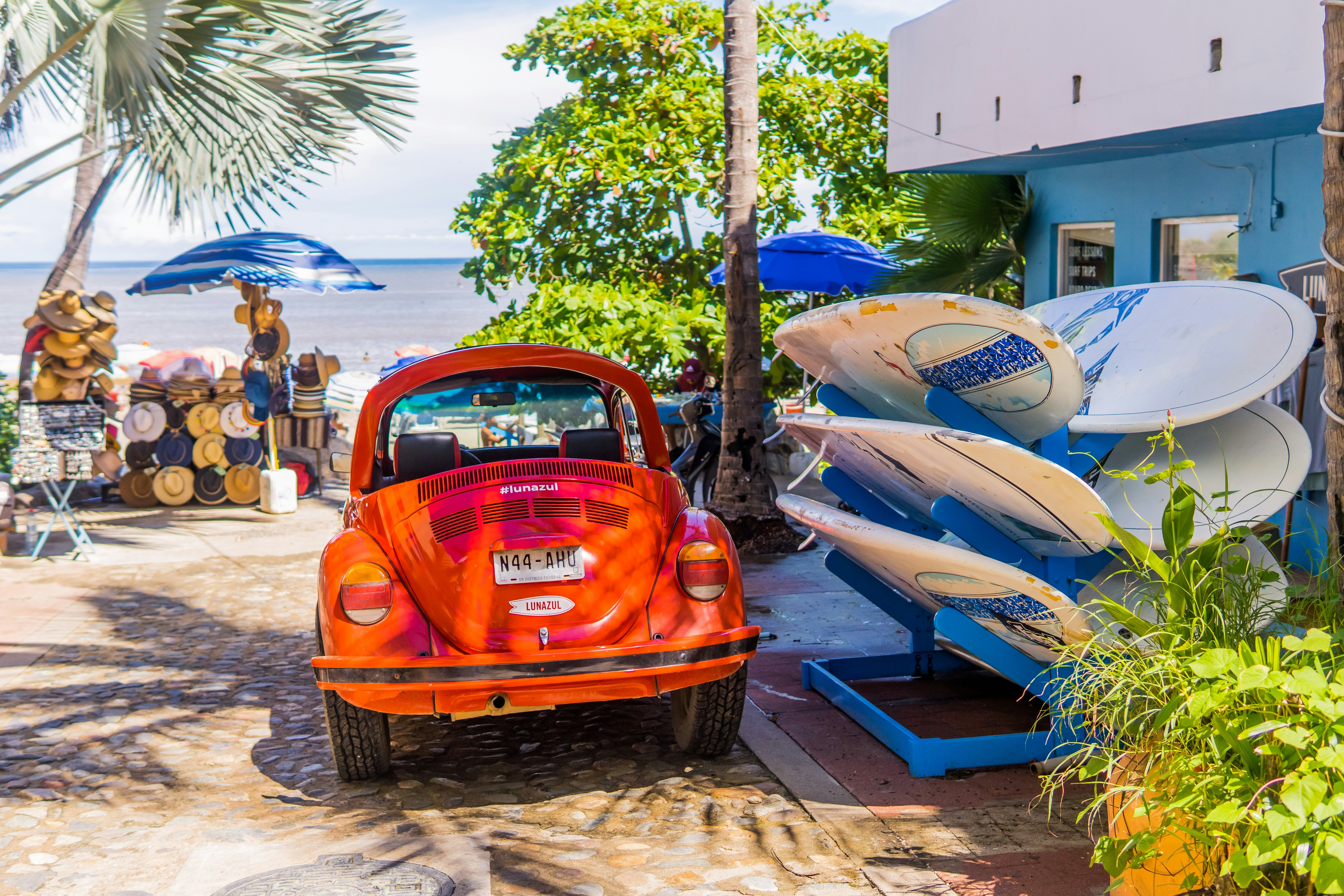 Klasikinis raudonas „VW Beetle“ („Vocho“) yra pastatytas šalia banglenčių už kelių pėdų nuo paplūdimio