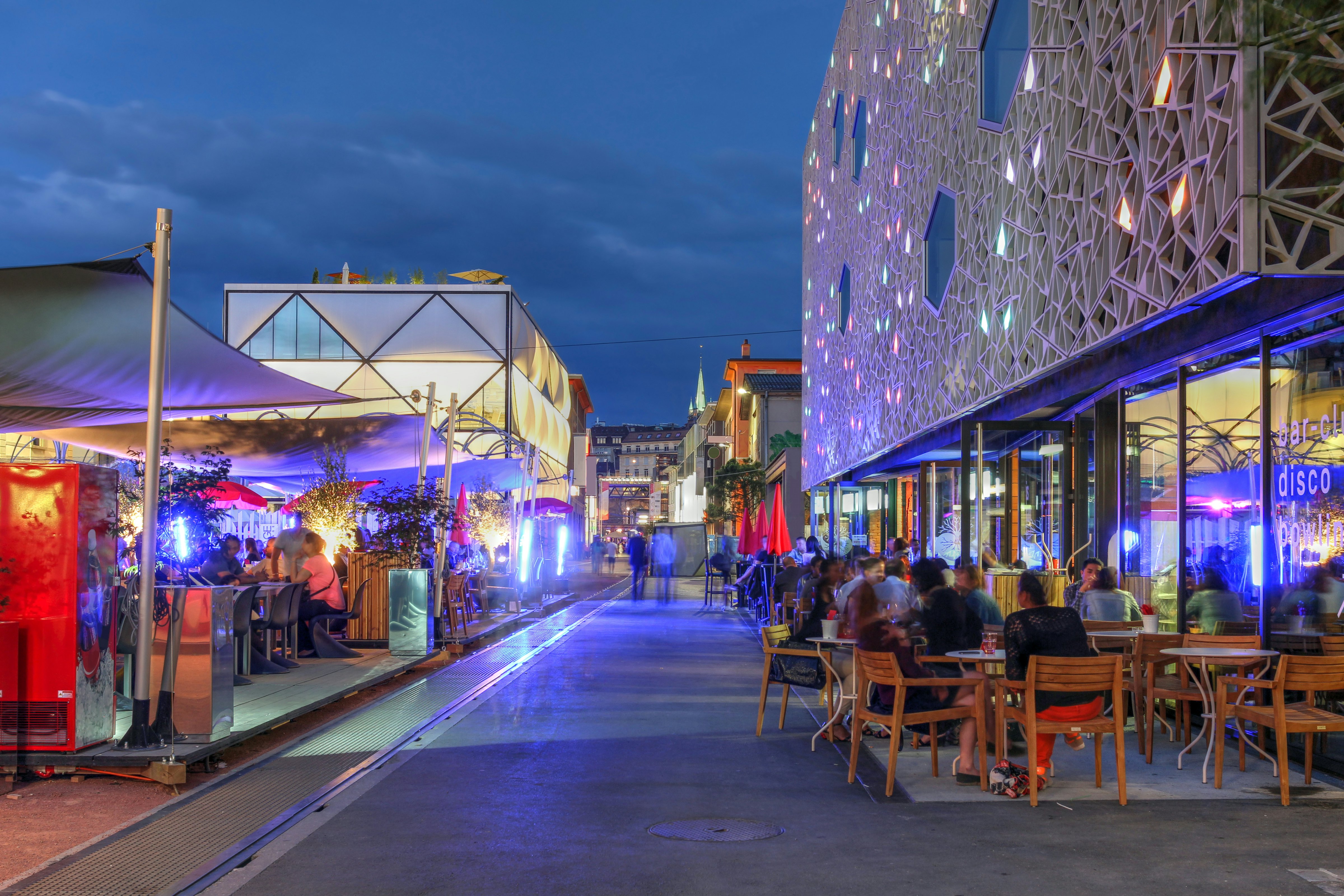 Naktinė scena mieste su žmonėmis sėdėjo už kavinių ir barų moderniame rajone