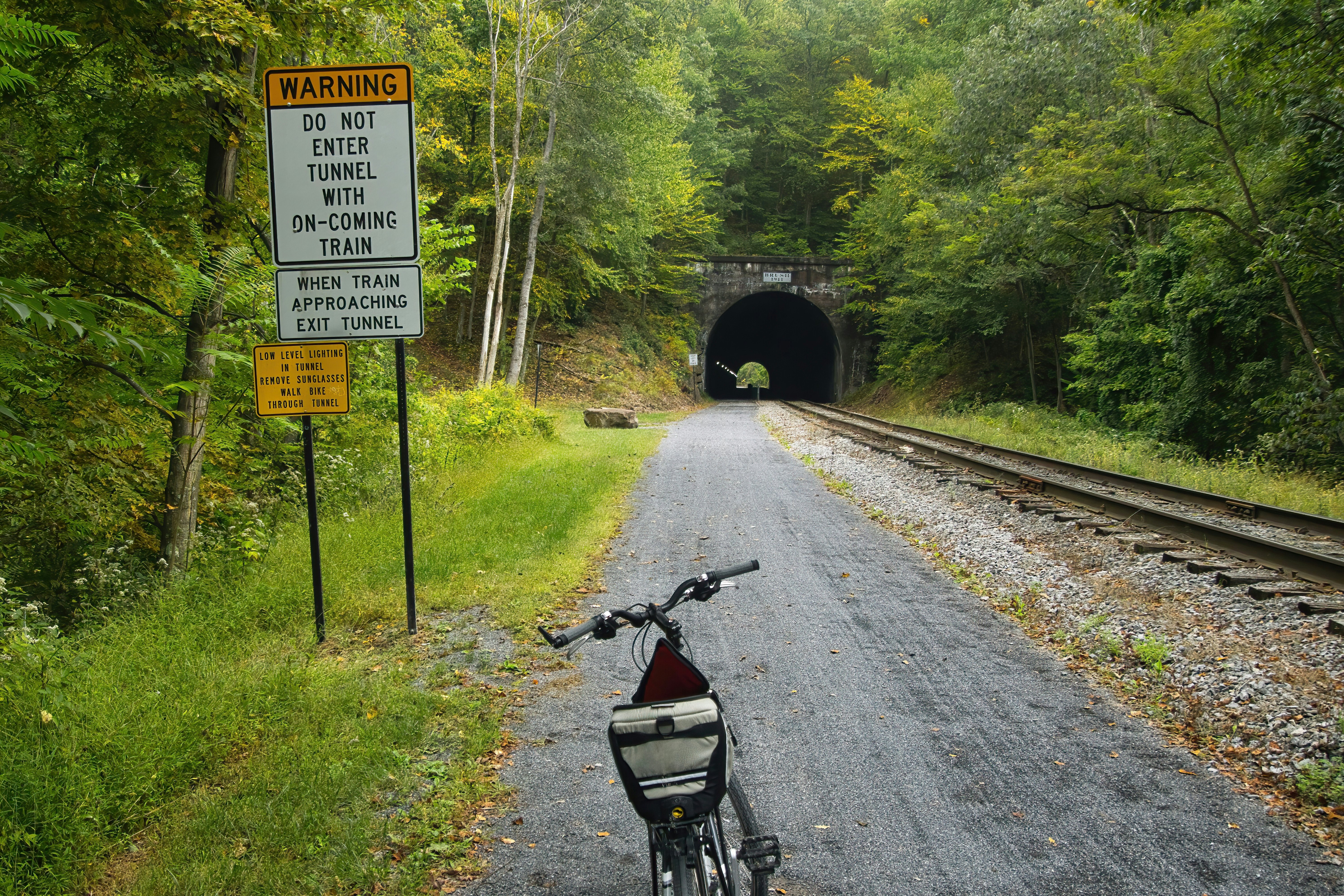 Landscape of a bike parked near a warning sign at the approach to a tunnel on the Great Allegheny Passage recreational trail, Pennsylvania