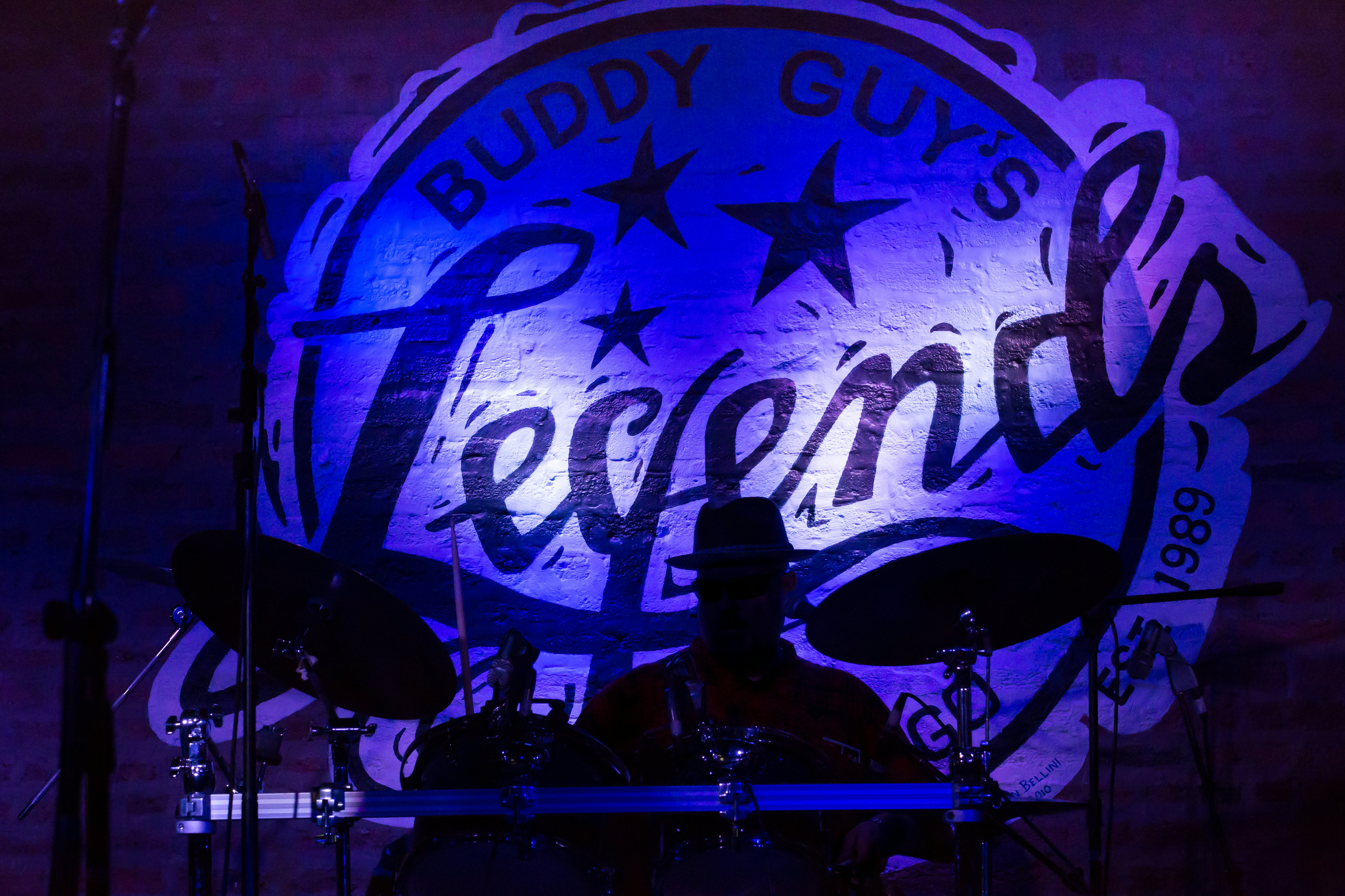 Būgnininkas scenoje Buddy Guy's Legends džiazo klube Čikagoje, apšviestas mėlyna šviesa.