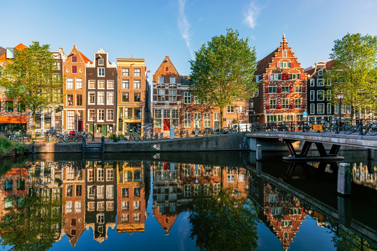 Seni istoriniai olandiški namai, atsispindintys kanale saulėtą dieną, Amsterdamas, Nyderlandai.