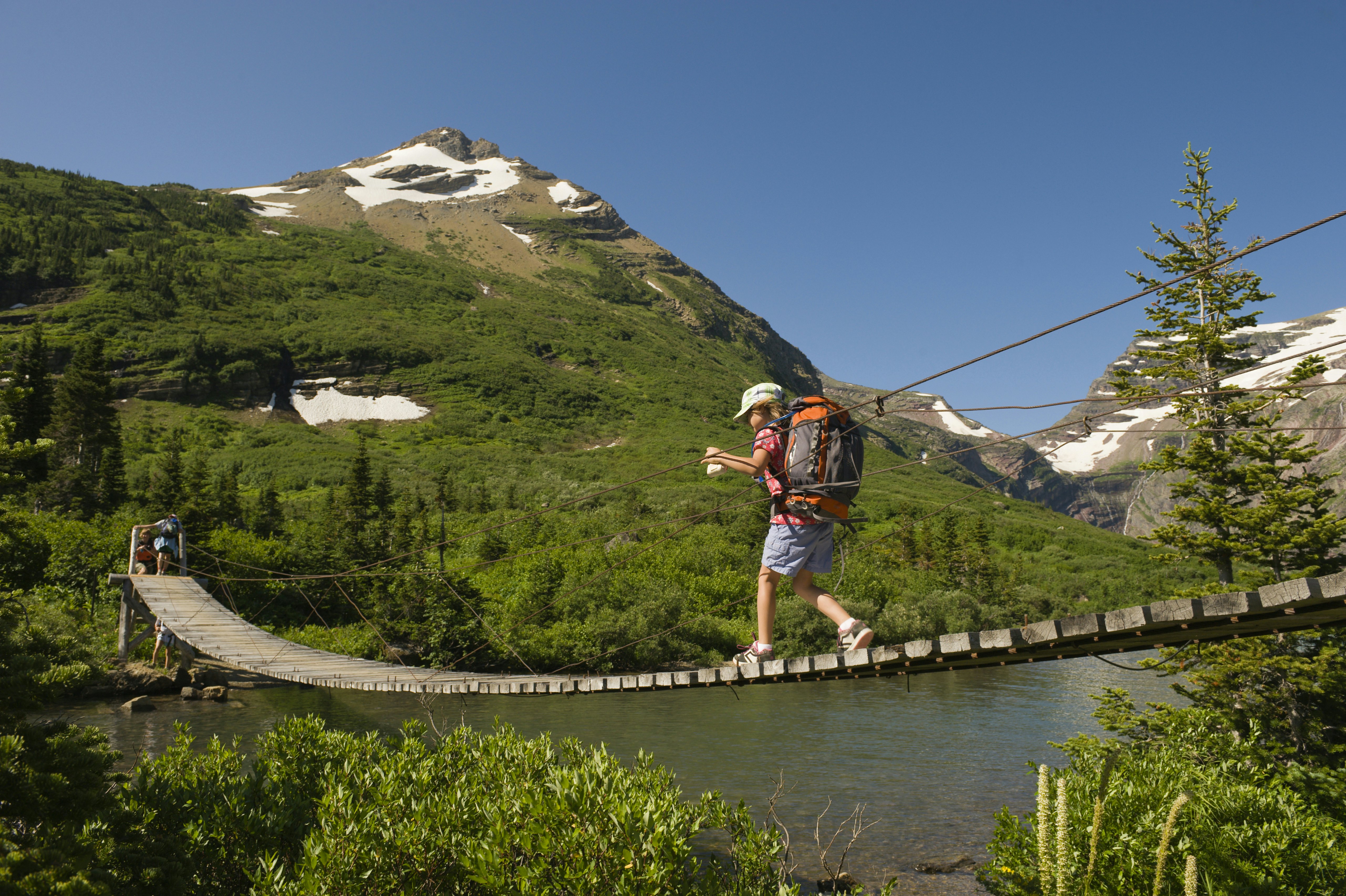 Mergaitė žygiuoja kabančiu tiltu Glaciaus nacionaliniame parke, Montana.