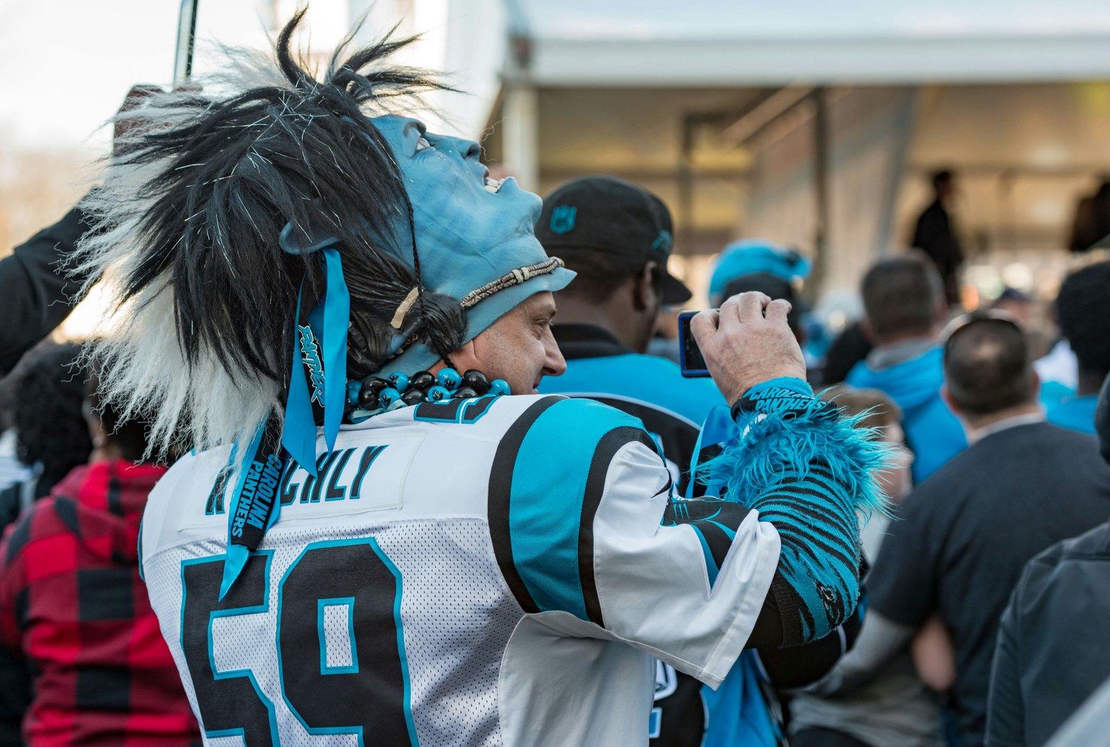 Carolina Panthers amerikietiško futbolo komandos gerbėjas, dėvintis marškinėlius ir kaukę, fotografuoja mobilųja