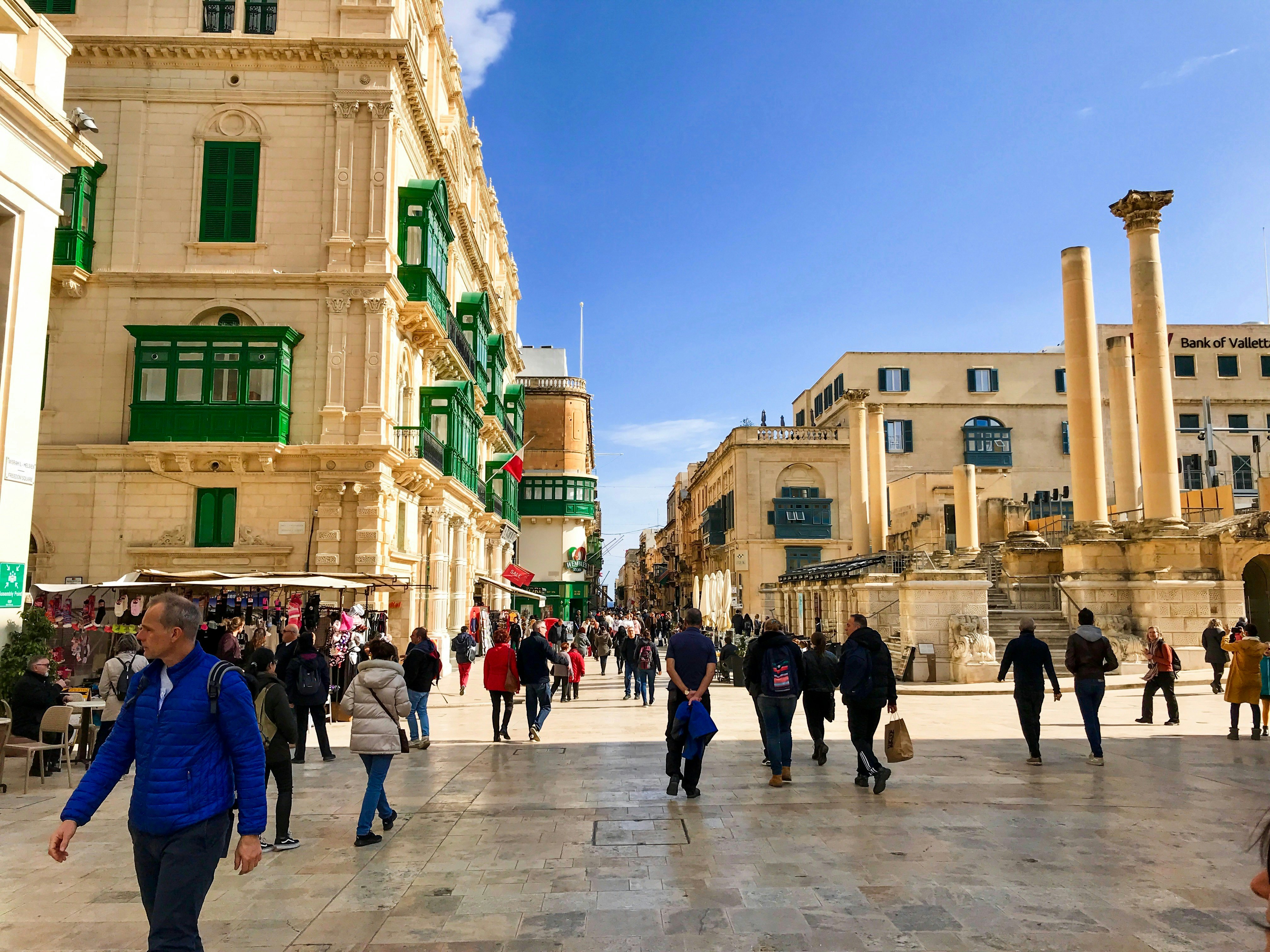 People walk around Valletta's historic centre on a sunny morning.