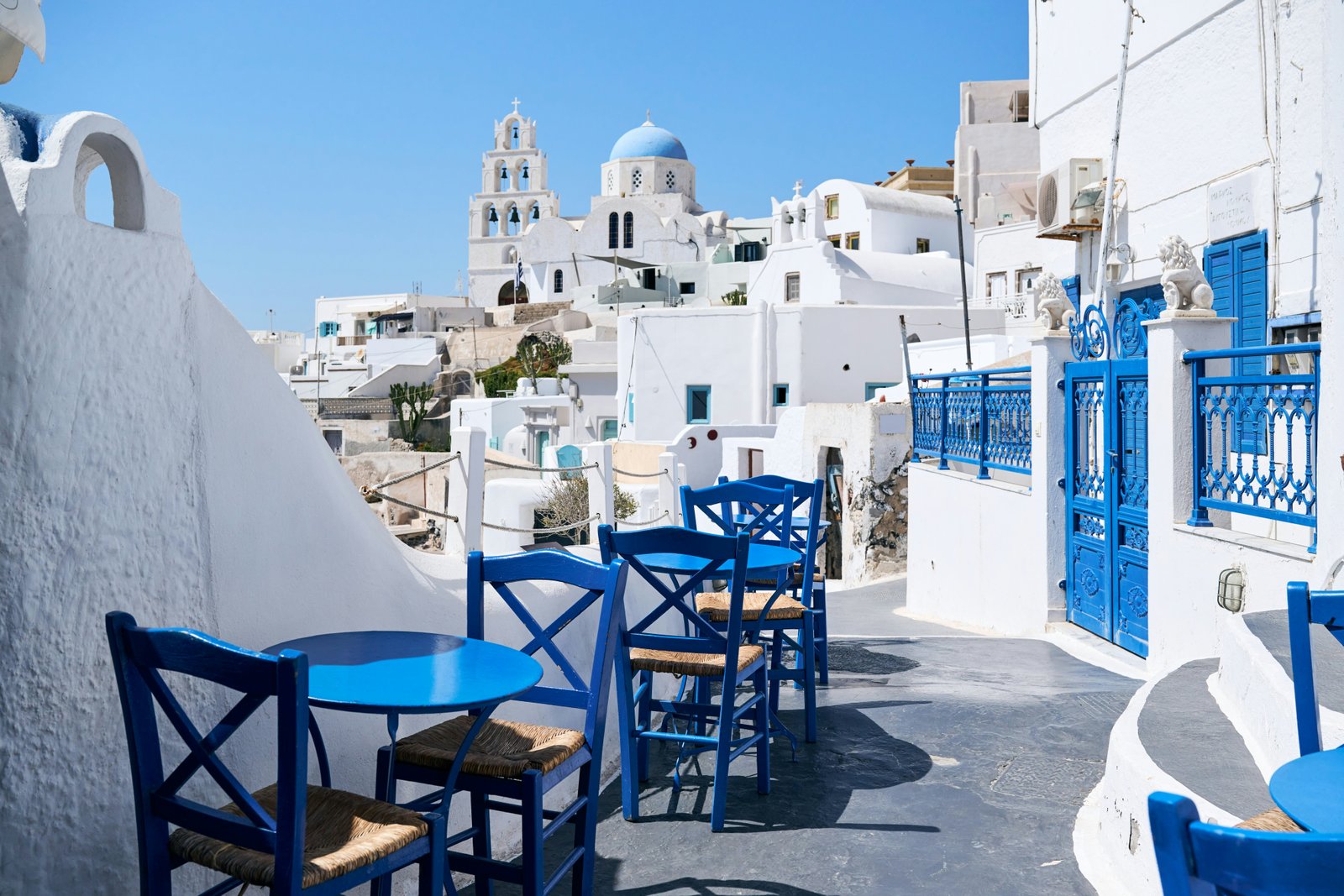A typical street with blue tables and chairs among white houses in Pyrgos on the Greek island of Santorini.
