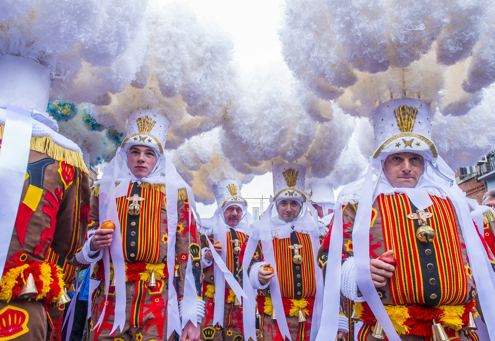 Žmonės išradinguose kostiumuose, kurie dengia jų kūnus ir galvas, stovi drumstoje aplinkoje, kaip karnavalo parado dalis