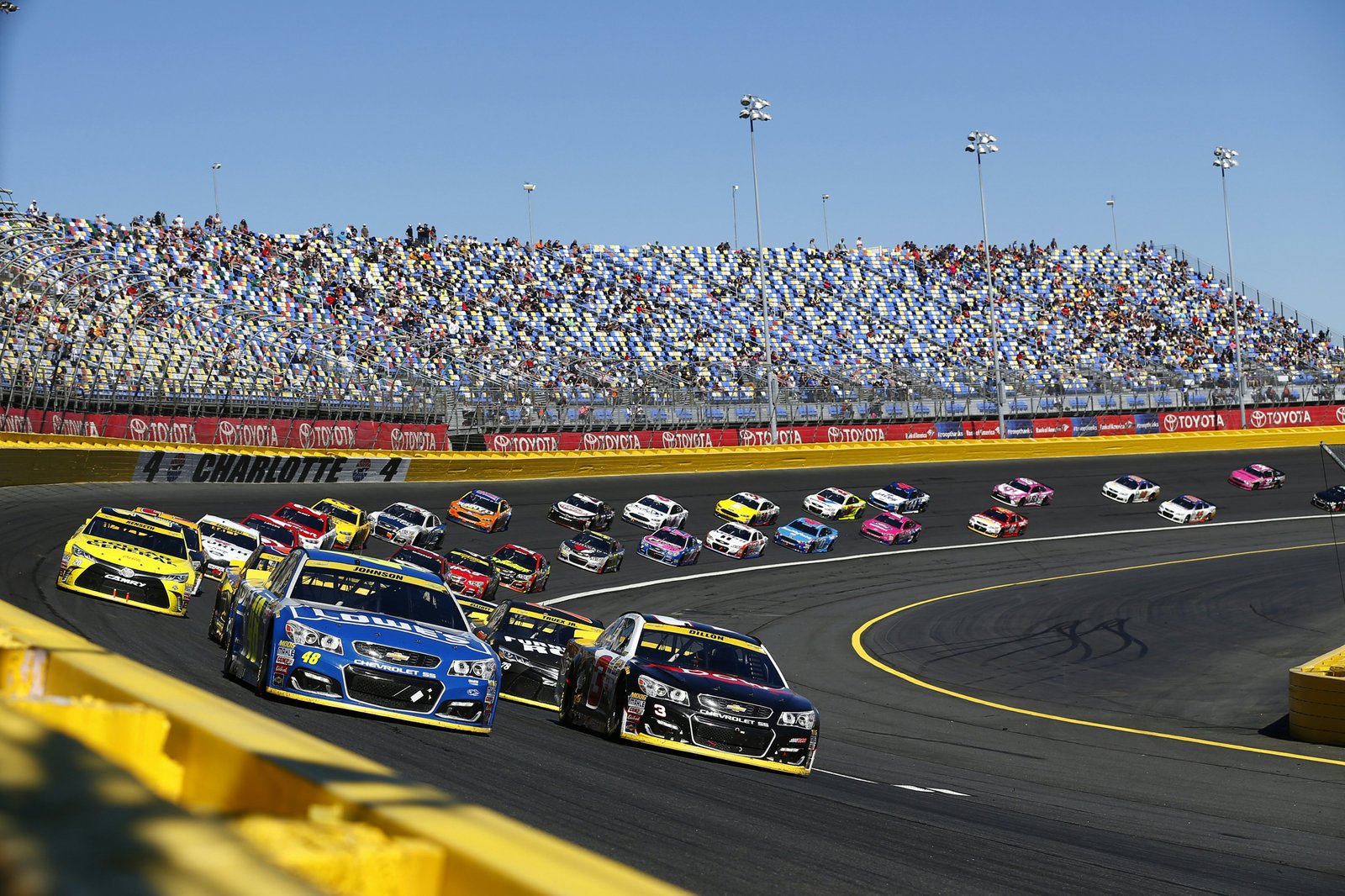 Lenktynių trasa su automobiliais, greitai lekiančiais pro sausakimšas žiūrovų tribūnas. Jimmie Johnson (48) ir Austin Dillon (3) pirmauja Bank of America 500 lenktynių metu Charlotte Motor Speedway trasoje Concord miestelyje.