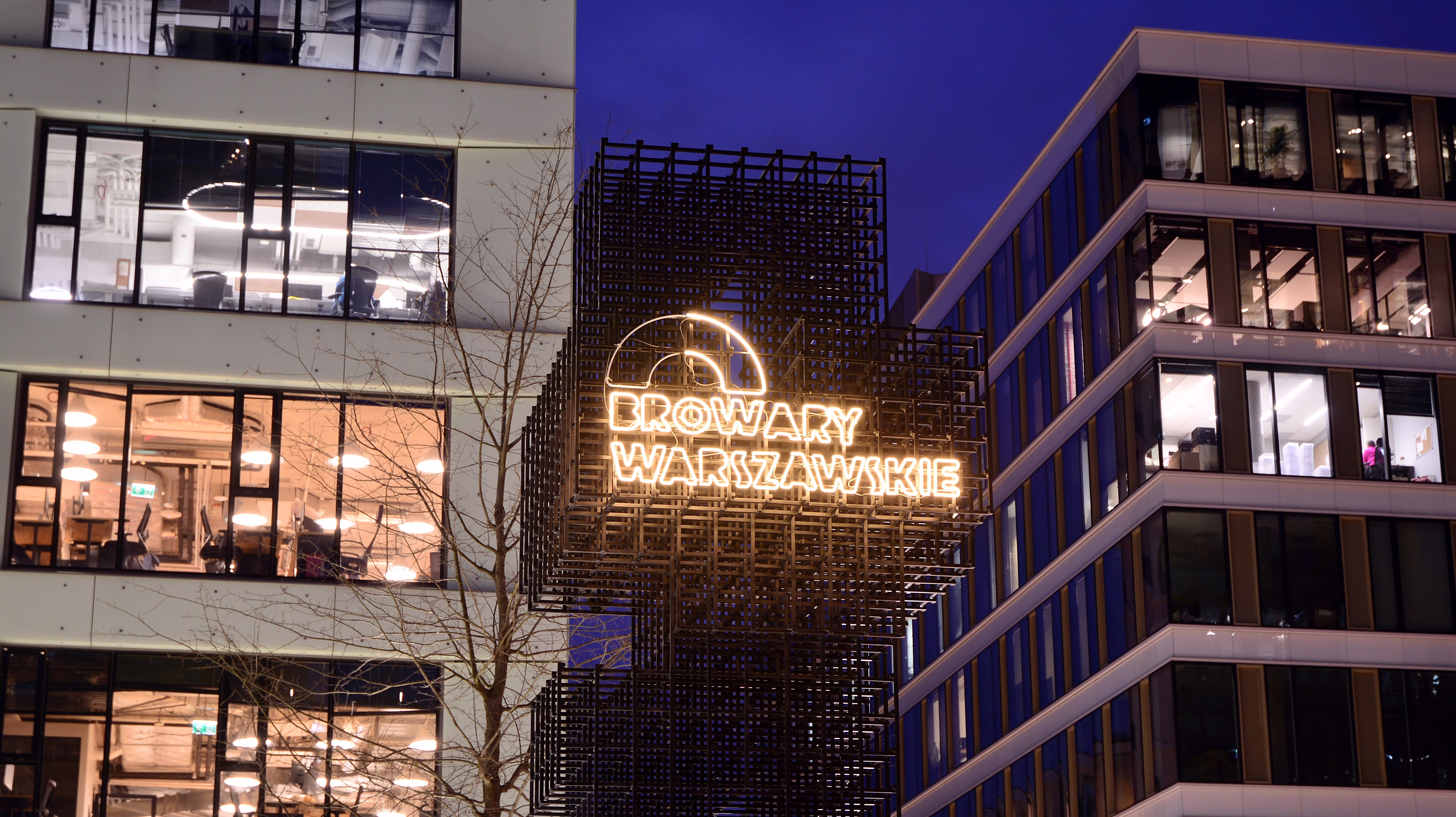 The exterior of an entertainment district at night, with a lit-up sign that says "Browary Warszawskie"