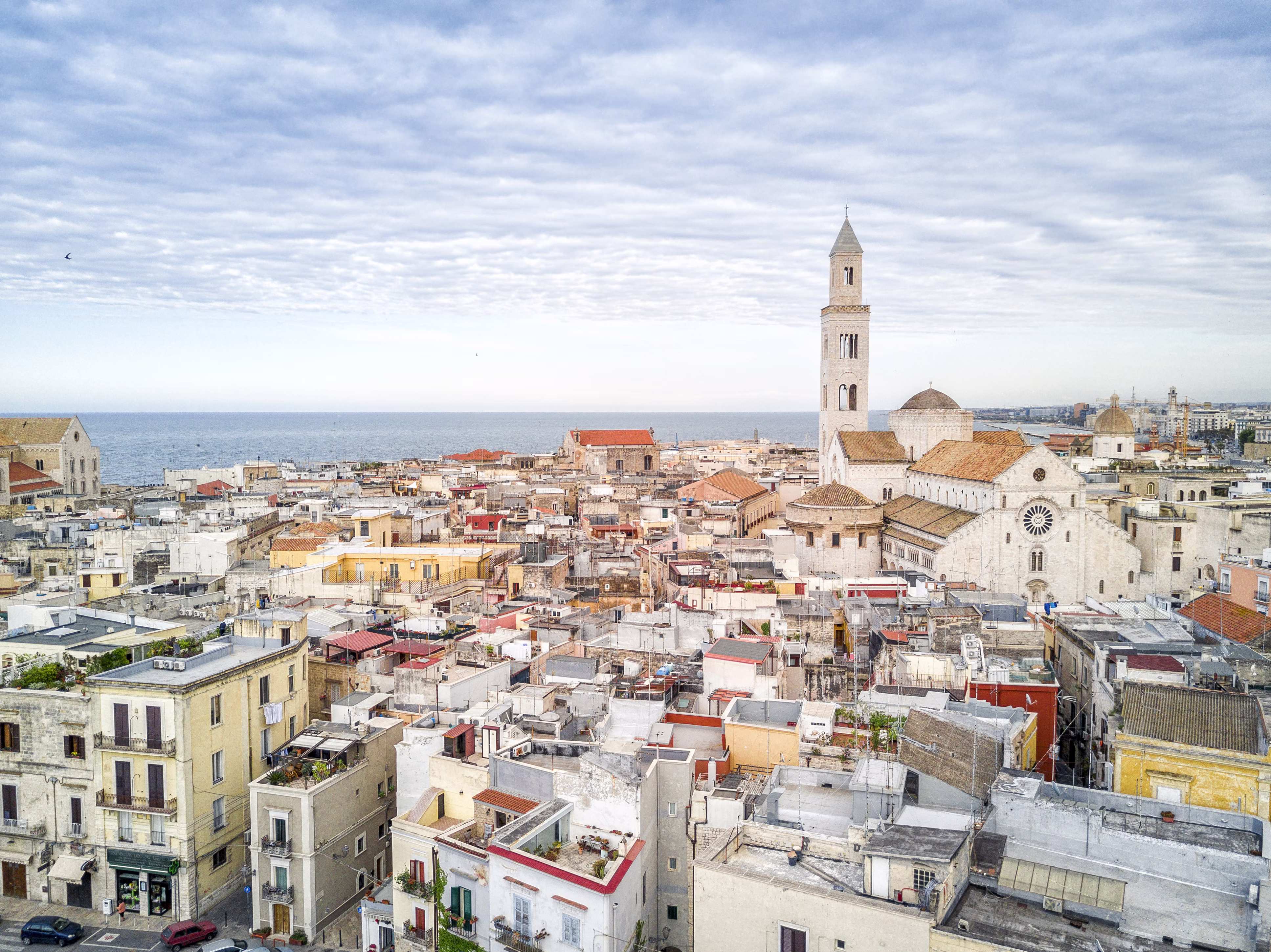A view of the tightly packed buildings of Bari Vecchia, with the spire of the Basilica di San Nicola and the sea in the distance.