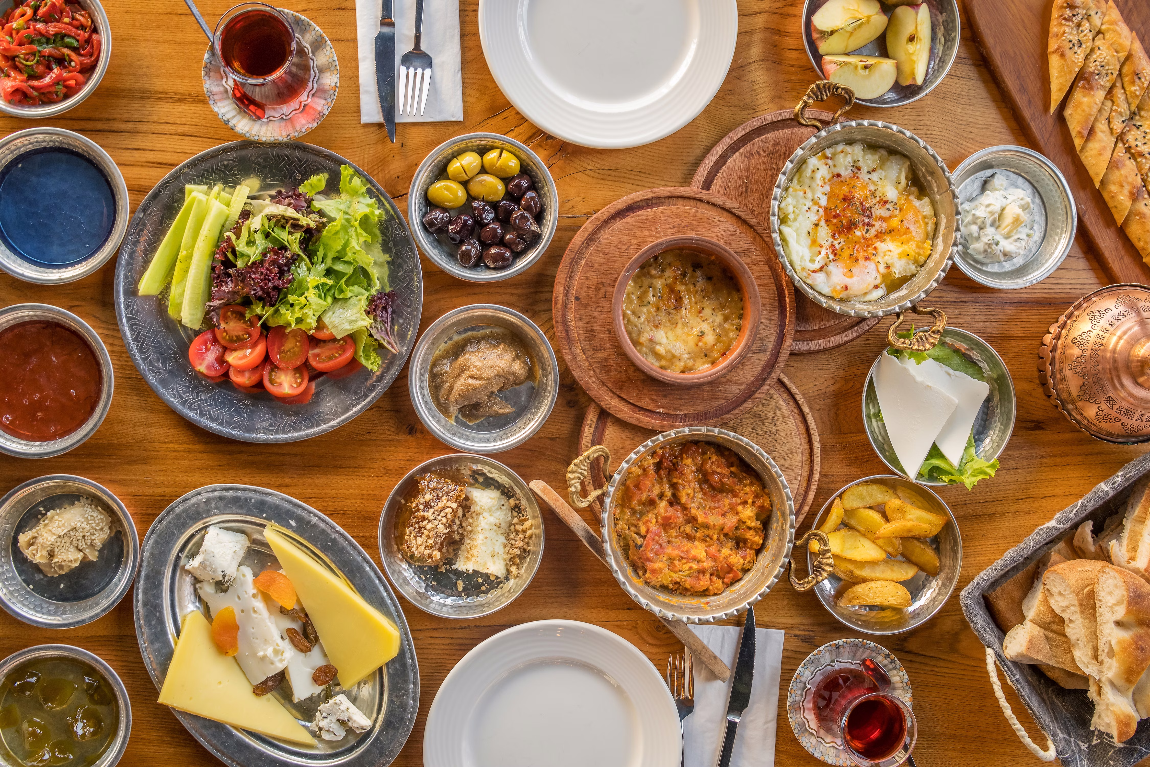 An overhead view of many dishes on a wooden table, including cheese, dips, bread and vegetables.