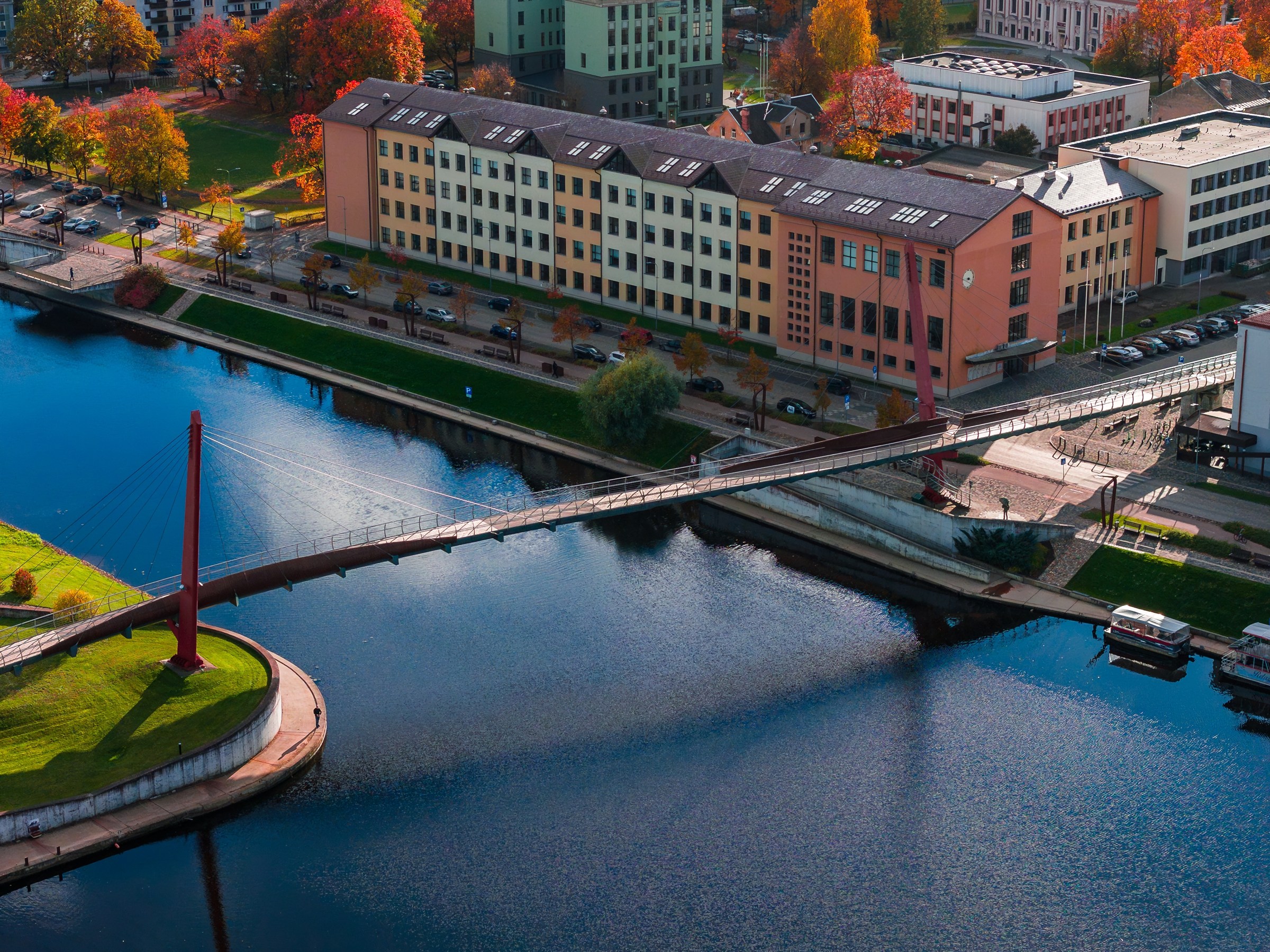 Iš oro matomas Mitavos pėsčiųjų tiltas per Driksą ir Jelgavos krantinės pastatai rudenį.